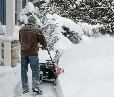 Residential snow removal technician using a snow blower to clear a home driveway and walkway in Boston, MA