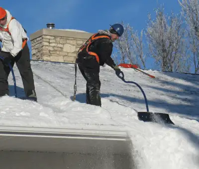 Professional technicians performing roof snow removal with safety harnesses and shovels in Boston, MA